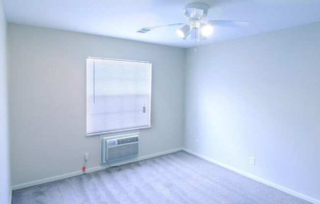 Bedroom with white walls, grey carpet, a ceiling fan, large window, and AC unit.