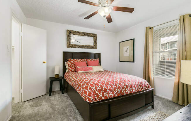 A bedroom with a bed, a ceiling fan, and a window with curtains.