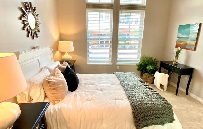 A bedroom with two tall windows, plush carpet flooring, and a ceiling fan.