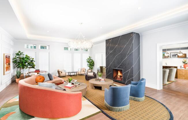 Spacious community lounge with a statement fireplace, curved seating, and soft lighting creating a welcoming space for gathering and relaxed conversation.