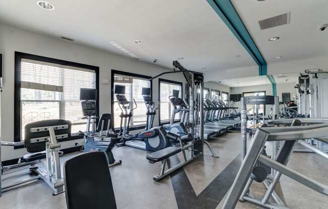 a large fitness room with cardio equipment and windows