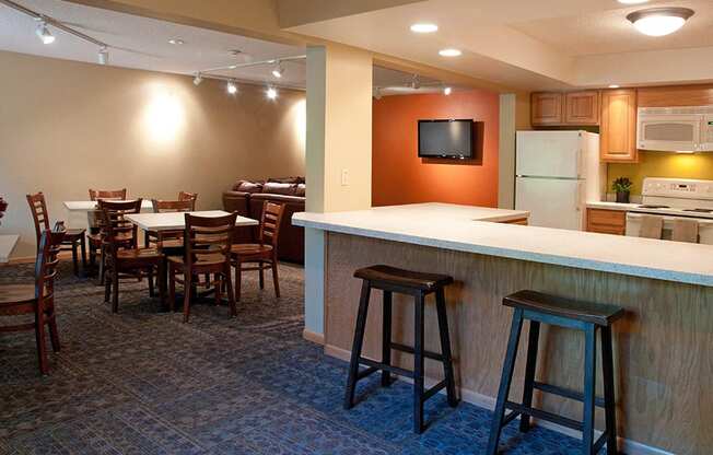 Community room with kitchen, bar seating, and square tables