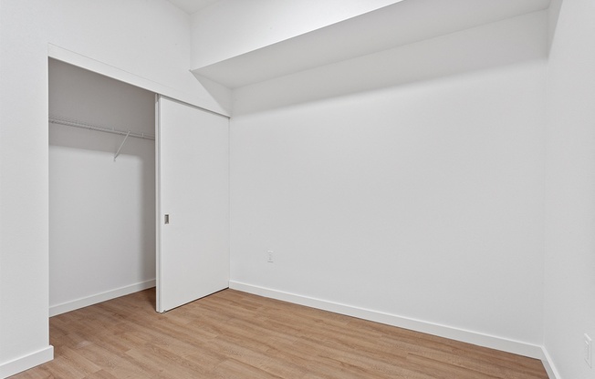 a bedroom with white walls and wood flooring and a closet
