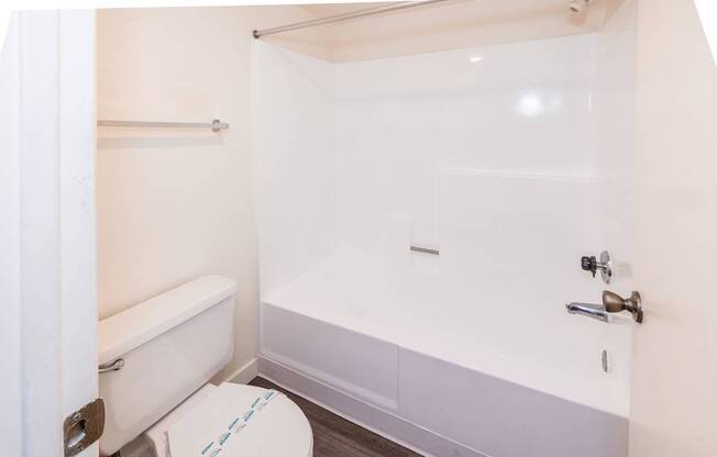 A white toilet with a blue line on the lid is in a small bathroom with a white bathtub and a white shower curtain.