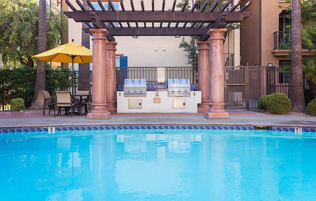 an outdoor kitchen next to a swimming pool with a hot tub and a pergola