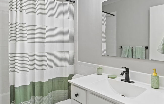 a white bathroom with a green and white striped shower curtain