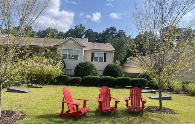 three red chairs sitting in a lawn in front of a house