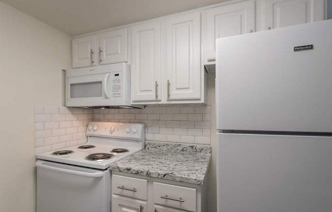 A kitchen with a white cabinets and white appliances 1 bedroom, 1 bath apartment home at Princeton Court Apartments in the Vickery Midtown neighborhood of Dallas, TX.