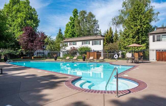 A large outdoor swimming pool surrounded by trees and a white building.