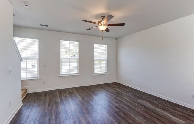 Townhouses for Rent in North Charleston, SC - Highland Townhomes - Empty Living Room with Hardwood Floor, Multiple Windows, White Walls, and Ceiling Fan.