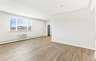 Bright and airy living space with large window, sleek hardwood floors, and modern kitchen entryway.