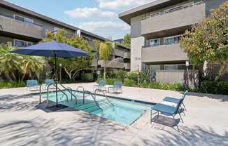 a swimming pool with chairs and an umbrella in front of a building