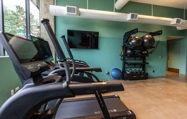 a gym with cardio equipment and a tv in the corner