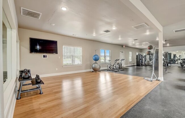 a large fitness room with hardwood floors and a flat screen tv on the wall