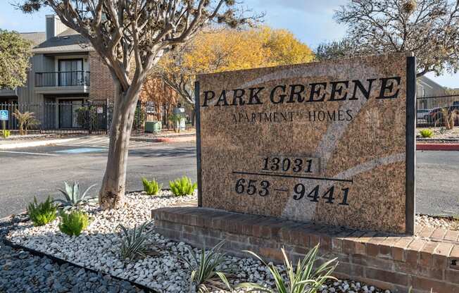 A sign for Park Greene Apartment Homes is displayed in front of a tree.