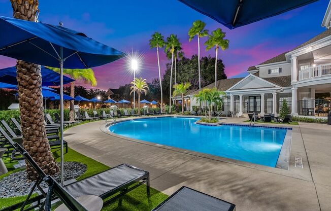 our resort style swimming pool is lit up at night with palm trees