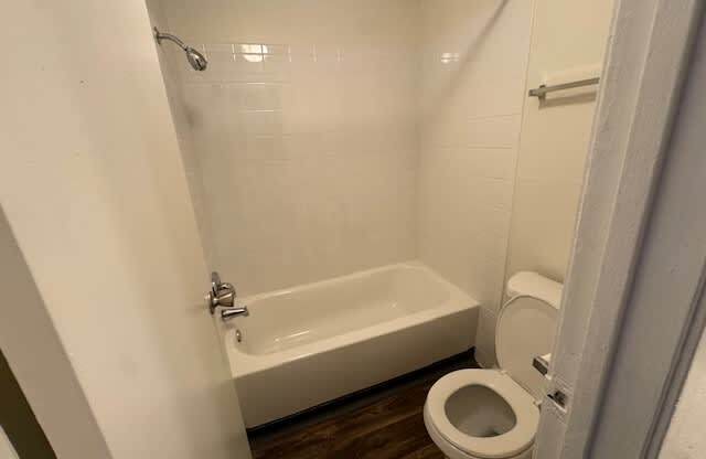 A white toilet is in a bathroom with a white tub.