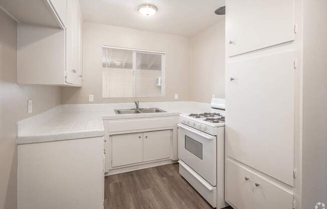 A white kitchen with a stove, sink, and cabinets.