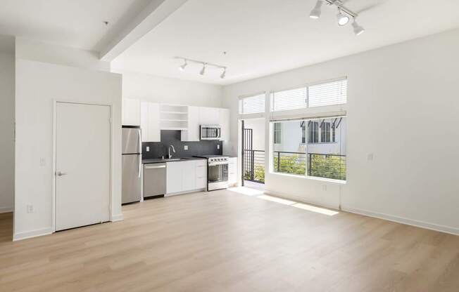 A spacious kitchen with white cabinets and appliances, a large window, and a wooden floor.