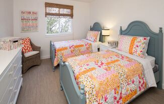 Bedroom with carpet floors, a white dresser, ceiling fan, and two full sized beds with colorful bedding.