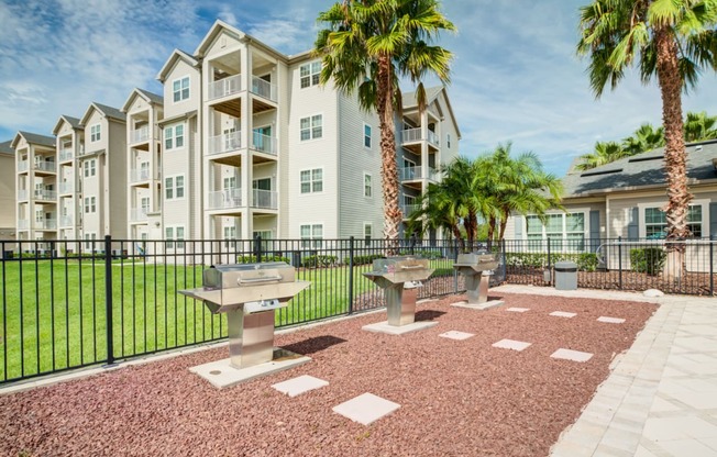 a patio with three bbq pits and two palm trees in front of an apartment building