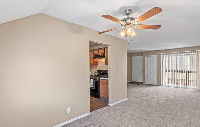 an empty living room with a ceiling fan and a kitchen