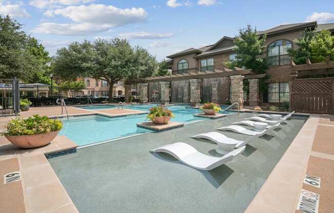 A large outdoor swimming pool with lounge chairs and a house in the background.