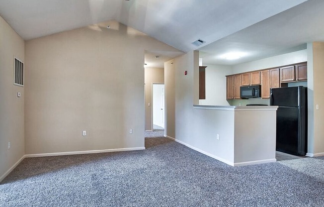 an empty living room with a kitchen and a ceiling fan