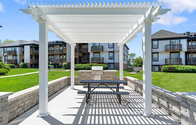 a picnic table under a white pergola in front of an apartment building