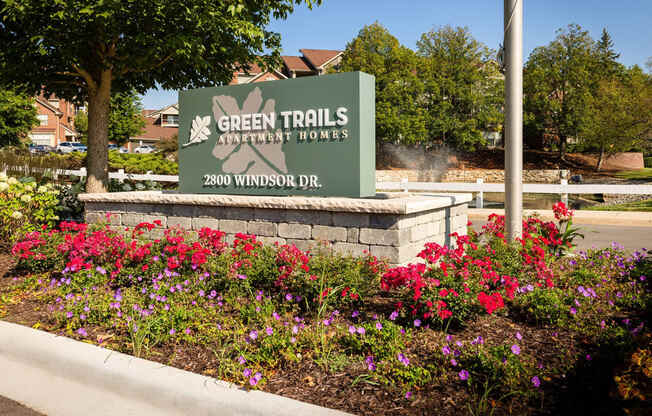 a sign for green trails amphitheatre hours in front of flowers