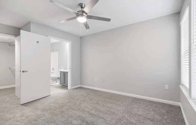 an empty living room with a ceiling fan and a door to a bathroom