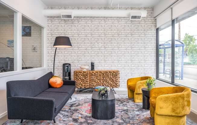 a living room with a black couch yellow chairs and a white brick wall