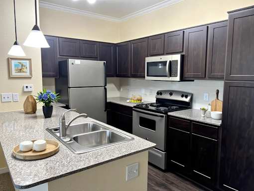 A kitchen with a refrigerator, microwave, oven, and sink.
