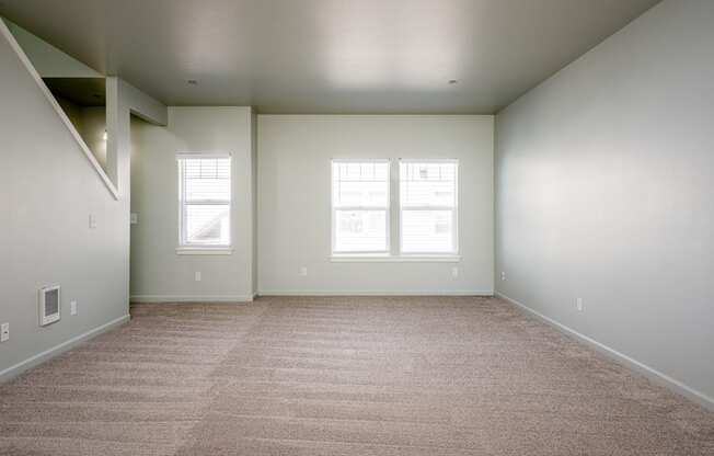 A large empty room with carpeted floor and two windows.
