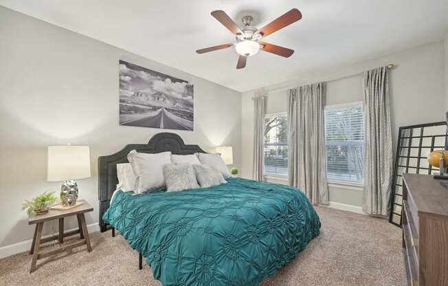 A bedroom with a bed, a ceiling fan, and a painting on the wall.