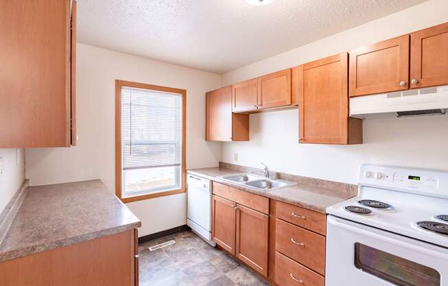 A kitchen with wooden cabinets and a white stove top oven. West Fargo, ND Sheyenne Terrace Townhomes