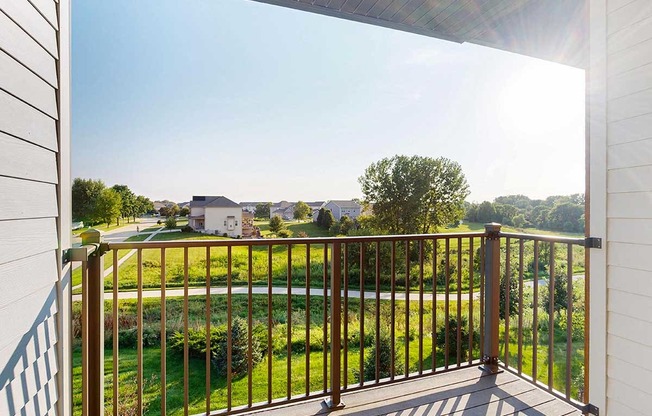 A balcony with a view of a green space, with houses in the distance.