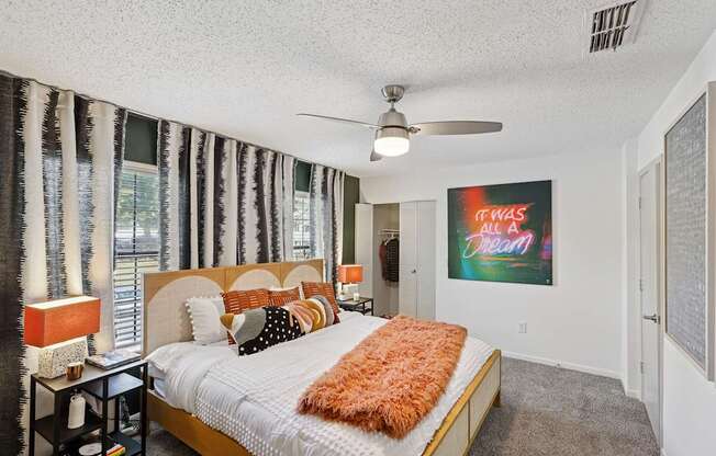 A bedroom with a bed, a ceiling fan, and a painting on the wall.