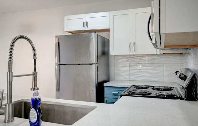 A kitchen with a stainless steel refrigerator, a sink with a blue bottle on it, and a stove with a white pot on it.