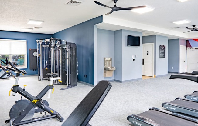 a gym with weights and cardio machines and a wall mounted tv