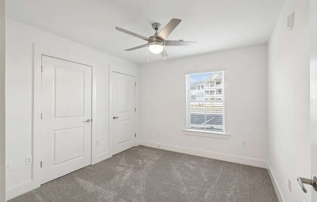 A room with a ceiling fan and a window with blinds.
