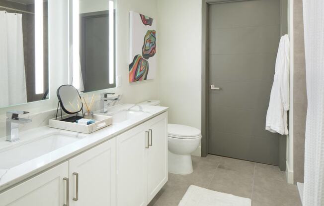 Studio Apartments in Woodland Hills, CA - The Q Variel - Bathroom with Custom Light-Framed Double Mirrors, Quartz Countertop Double-Sinks, and Tiled Flooring and Shower Walls