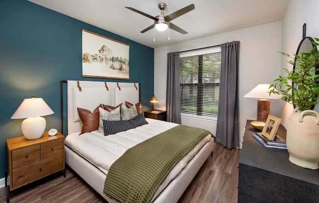 A bedroom with a bed, nightstand, and a plant.