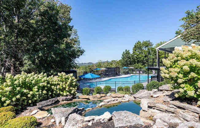 A pool surrounded by rocks and greenery with a house in the background.
