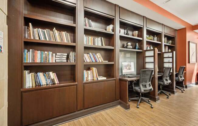A room with a long bookshelf filled with books and a desk with chairs.