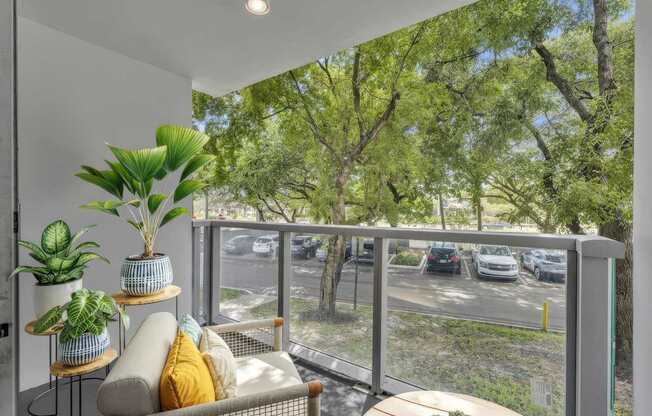 A balcony with a couch, plants, and a view of a parking lot.
