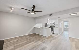 A spacious kitchen and living room with a ceiling fan and lighting fixture.