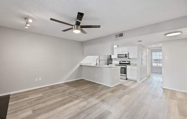 A spacious kitchen and living room with a ceiling fan and lighting fixture.