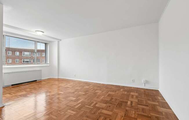 A room with wooden flooring and a window overlooking a building.