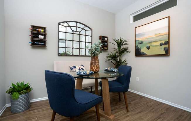 A dining room with a table, two chairs, and a painting on the wall.